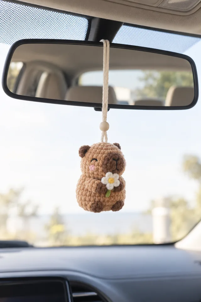 Concept IA d'un pendentif rétroviseur au crochet en forme de capybara marron tenant une marguerite blanche, suspendu à un cordon de perles